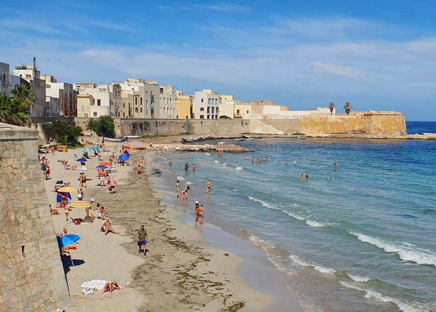 Narrow sandy beach backed by a high wall and the buildings of Trapani town centre