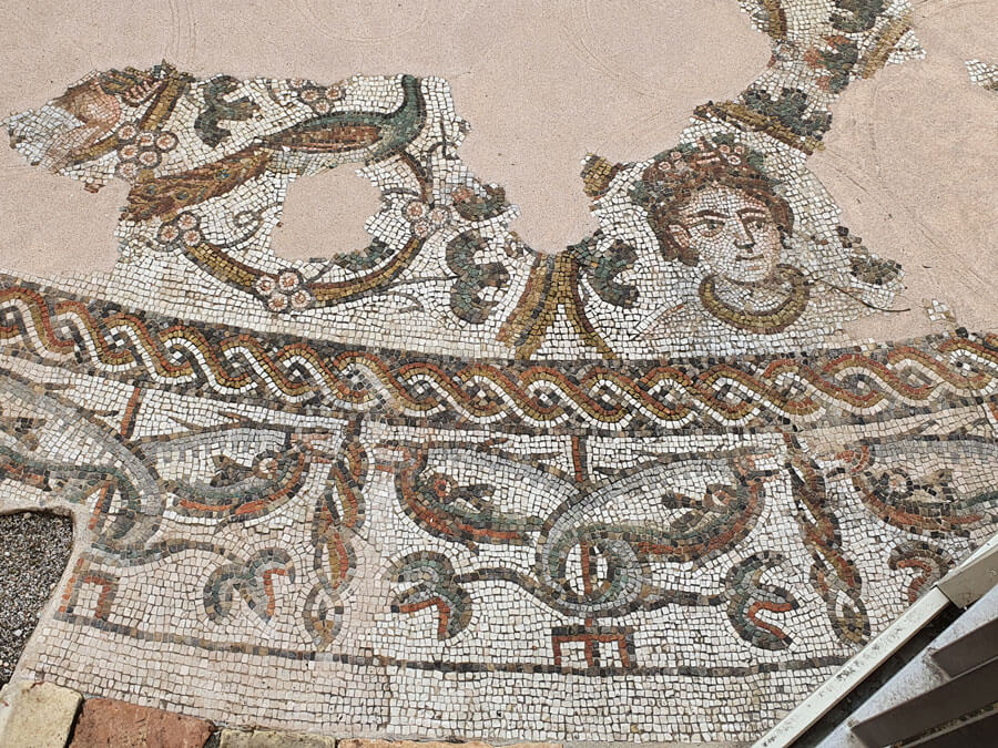 A fragmentary mosaic showing the face of a woman with flowers in her hair, a peacock and marine creatures