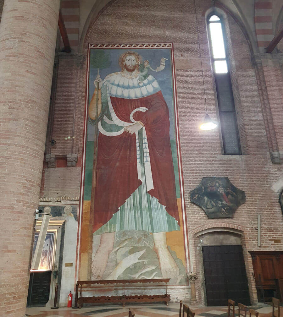 An interior wall of the church of San Nicolò in Treviso, featuring a huge wall-painting of St Christopher wearing a red robe, with fish swimming around his feet