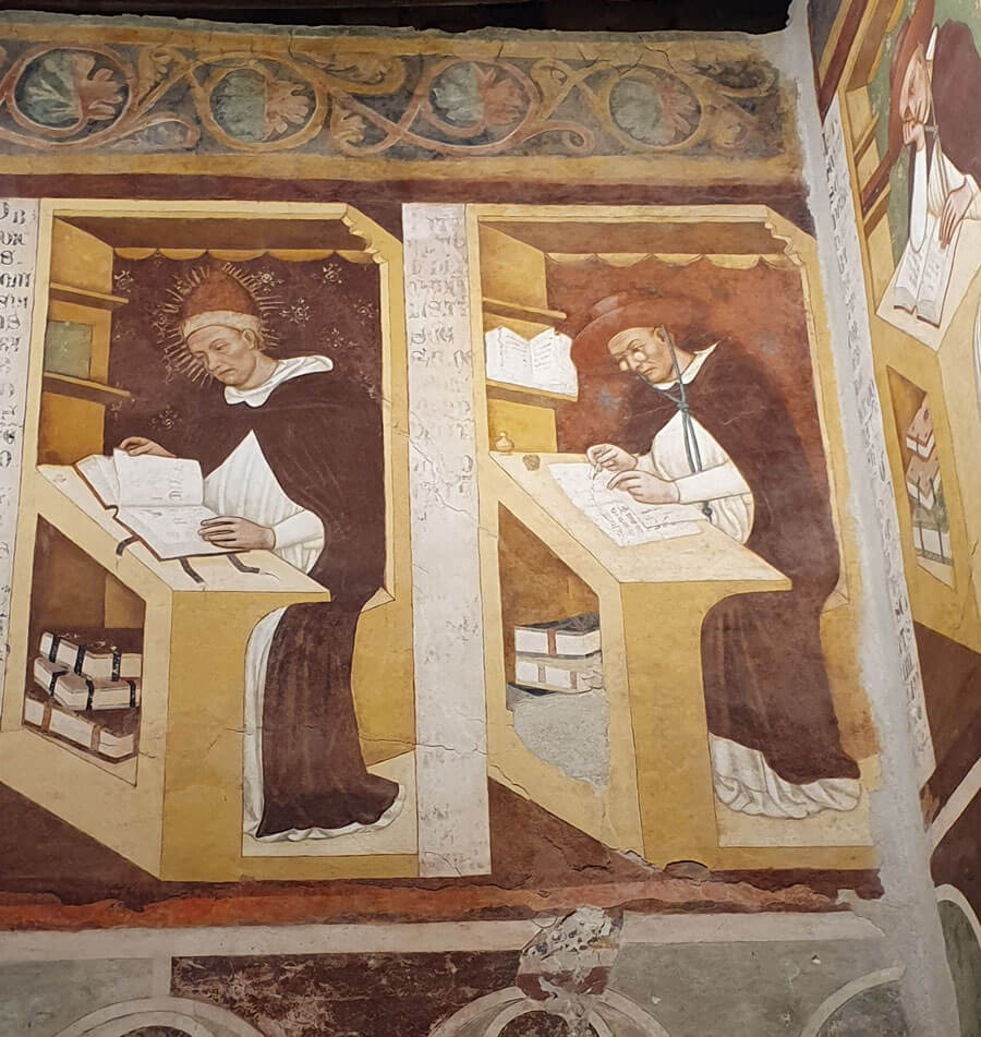 Wall-painting of two 14th-century monks sitting at desks working on books and manuscripts; one is wearing spectacles