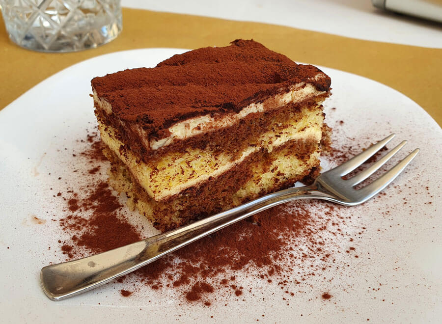 A helping of tiramisù on a plate with a fork alongside